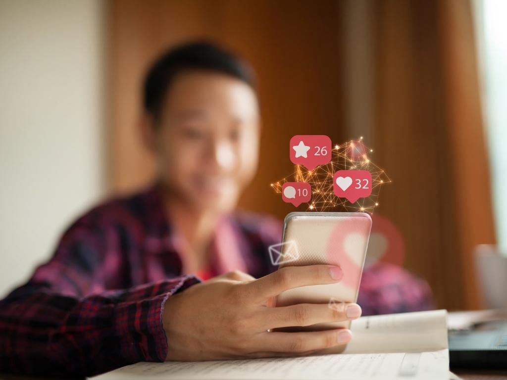 Person using a smartphone with social media icons, highlighting social media's role in off page SEO for landscapers