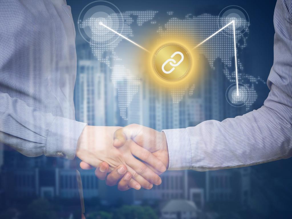 Two people shaking hands with a glowing link icon, symbolizing building relationships for quality landscaping backlinks